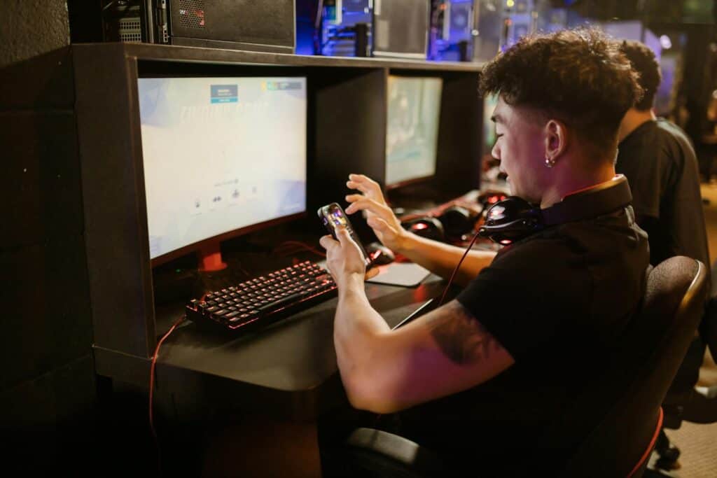 Man in Black Shirt Using a Smartphone while Sitting by the Gaming Computer