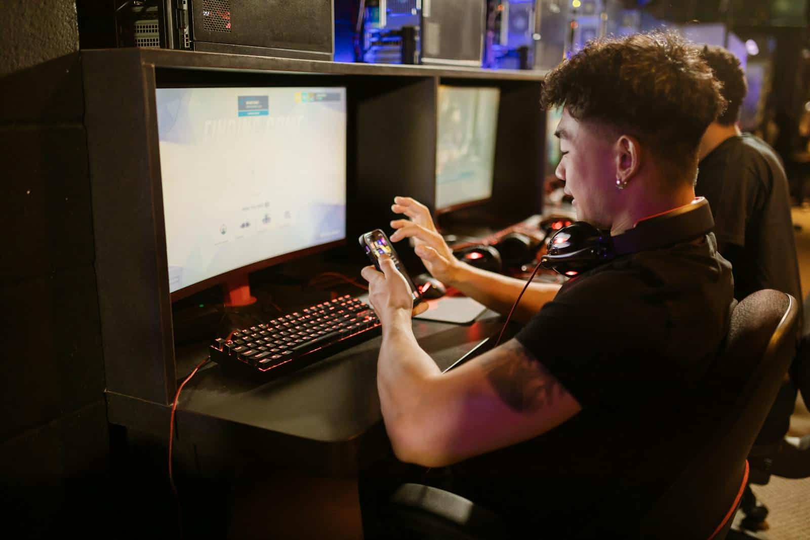 Man in Black Shirt Using a Smartphone while Sitting by the Gaming Computer